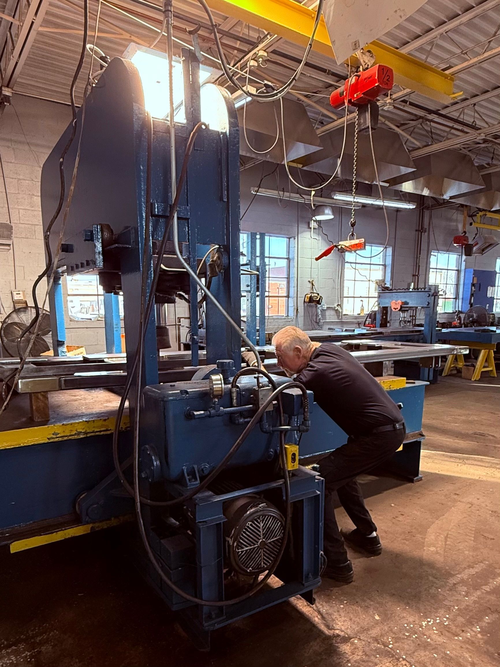 A person works on a large blue industrial machine in a factory setting.