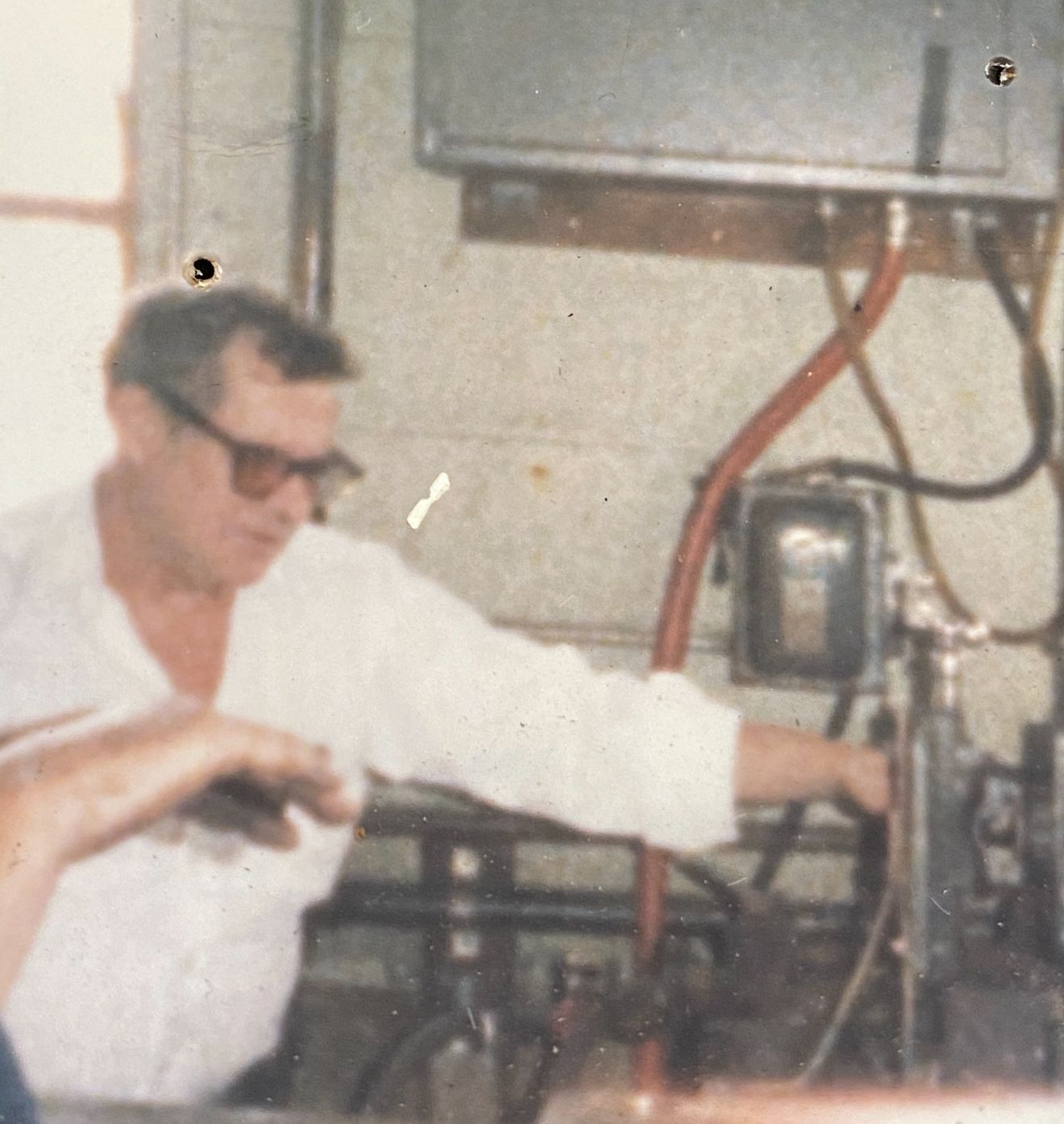Man wearing glasses works on machinery in a workshop.