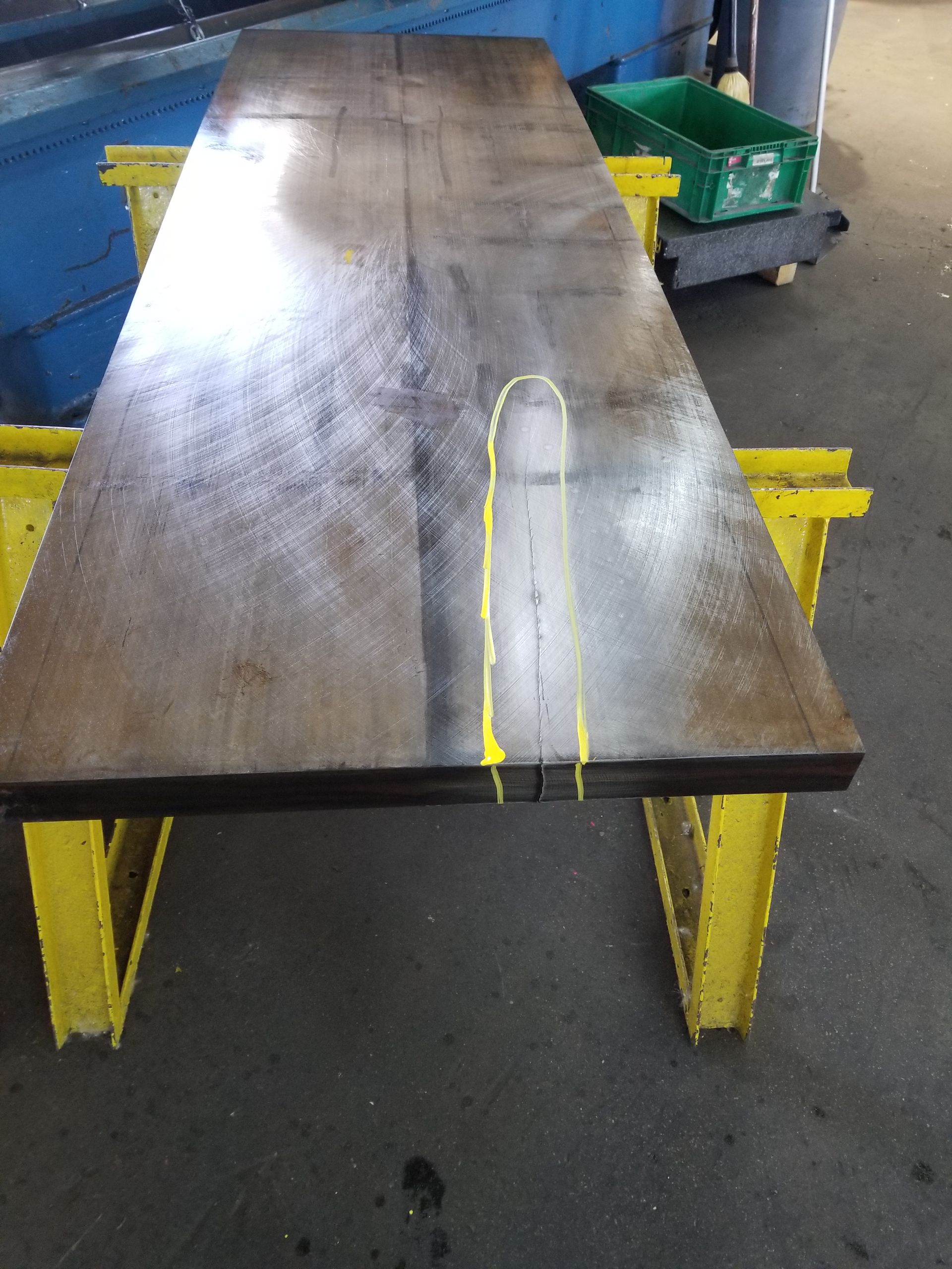 Large, rectangular metal table on yellow supports. Yellow markings indicate a cut line.