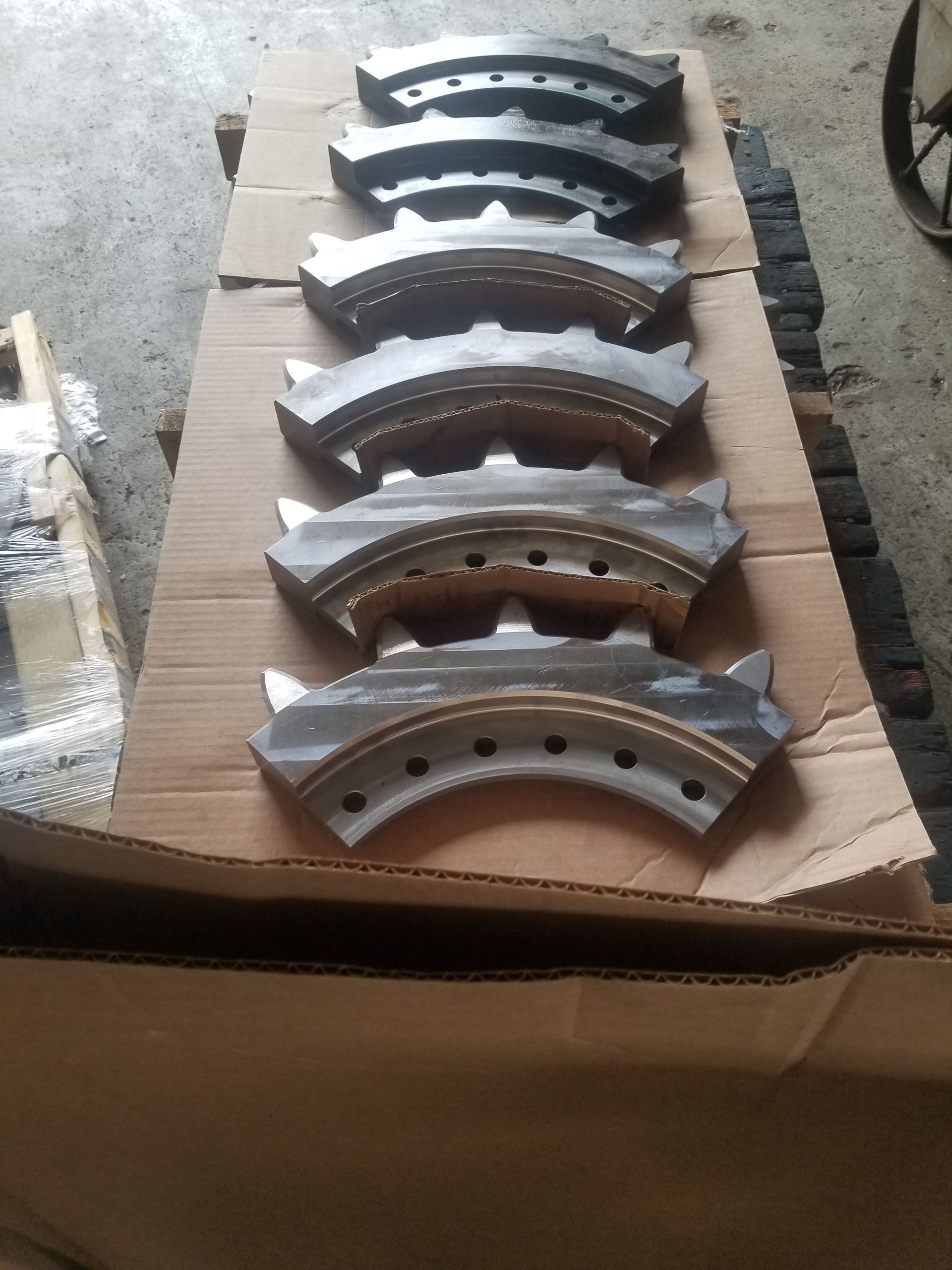 Six metal arc-shaped pieces with gear-like edges and holes, arranged on cardboard.