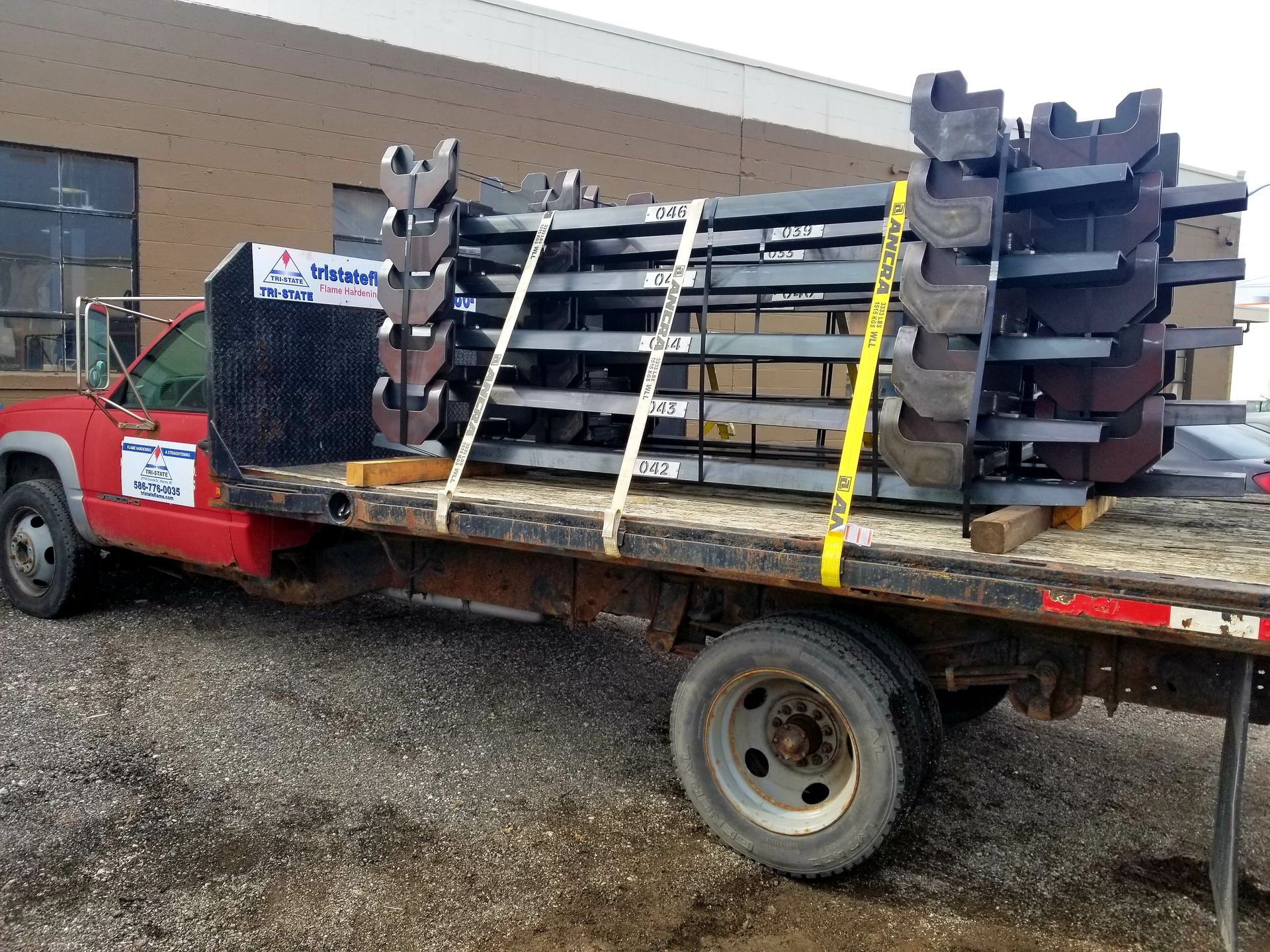 Red truck carrying a stack of metal beams secured with straps. Exterior shot, daylight.