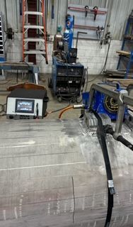 Welding equipment in a workshop setting, used on a large, metallic cylinder with a machine nearby.