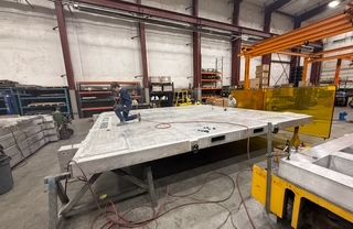 Person on large metal table in industrial setting. Welding shield nearby.