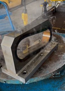 Metal bracket with a large oval opening, sitting on a rotating machine.