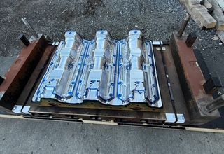 Metal mold with three cavities, bolted to a wooden frame, outdoors.