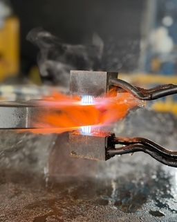 Metal being heated with bright orange flame between metal clamps. Steam rising.