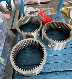 Three large, circular metal gears with internal teeth, on a blue pallet.