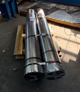 Two long, cylindrical metal objects, banded and on a wooden pallet, indoors.