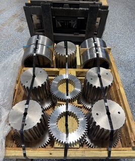 Gears and couplings on a wooden pallet, secured with straps. Industrial machinery components.