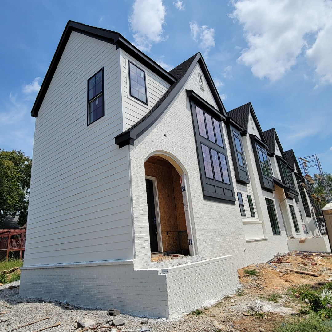 New construction home with light siding, dark windows, and a partially cleared lot.