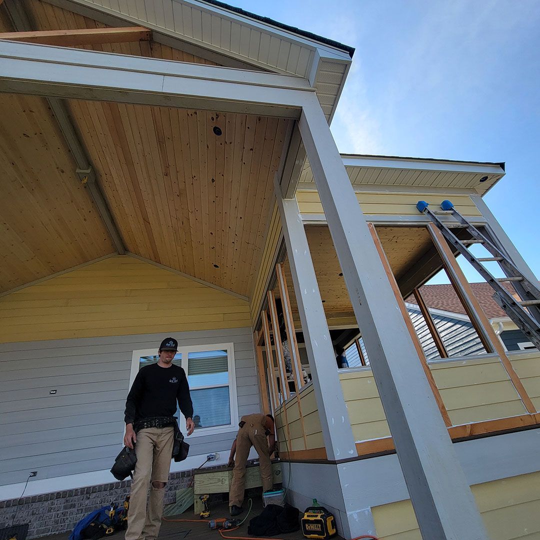 New house under construction with yellow siding, blue sky, and dirt foreground.