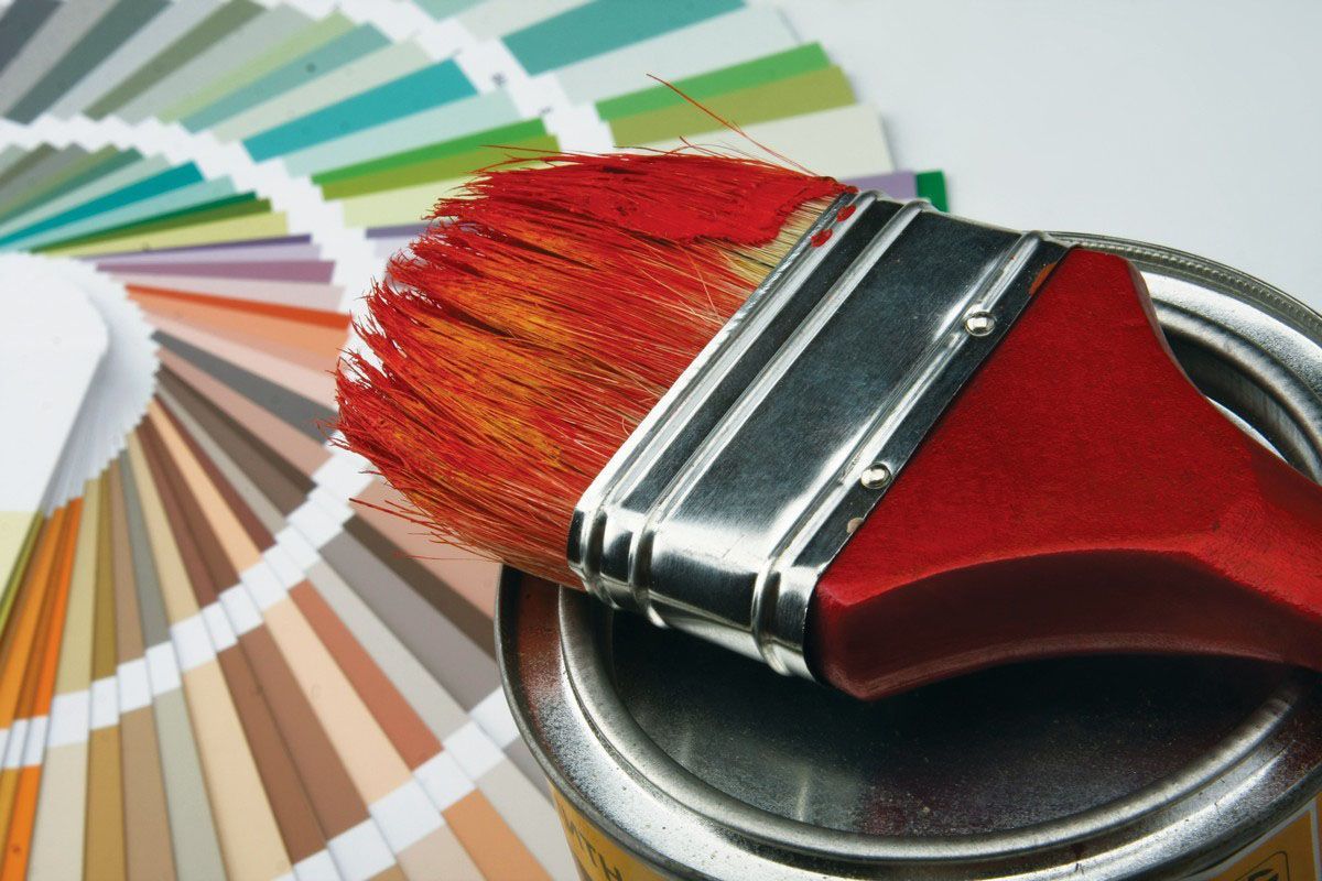 Paintbrush with red bristles on a paint can, next to a color swatch fan.
