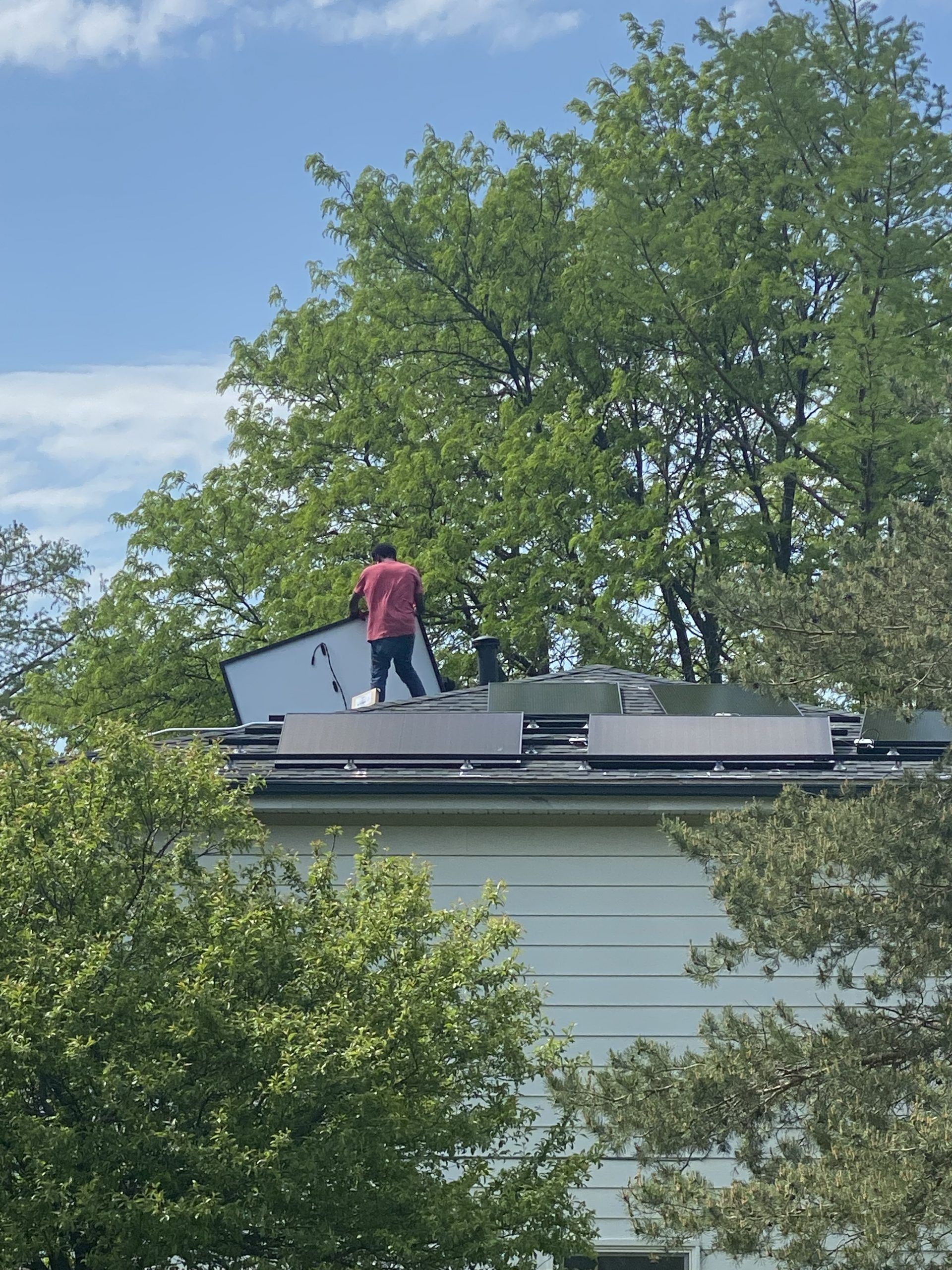 A man in a red shirt is standing on the roof of a house