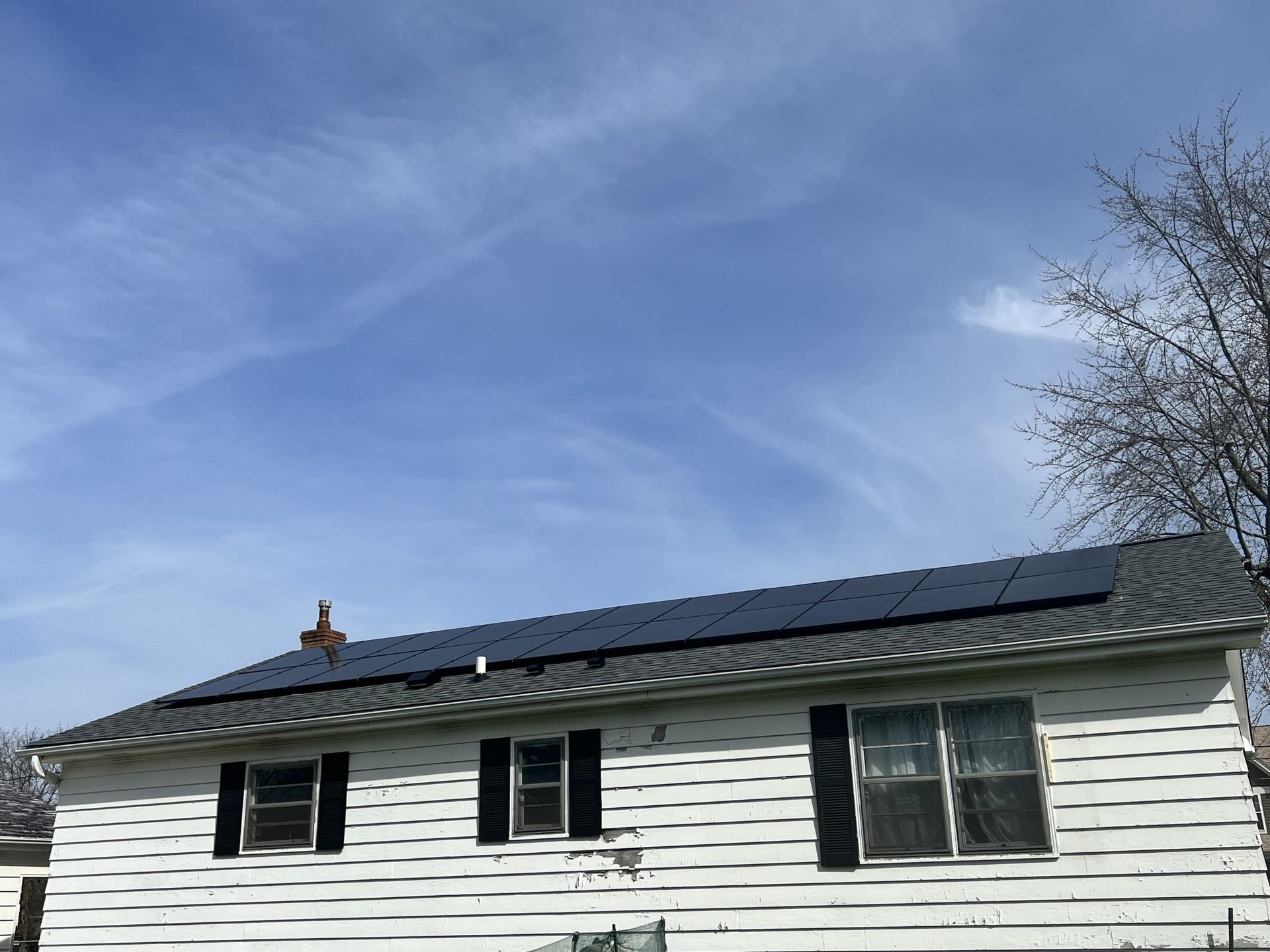 A white house with black shutters and solar panels on the roof.