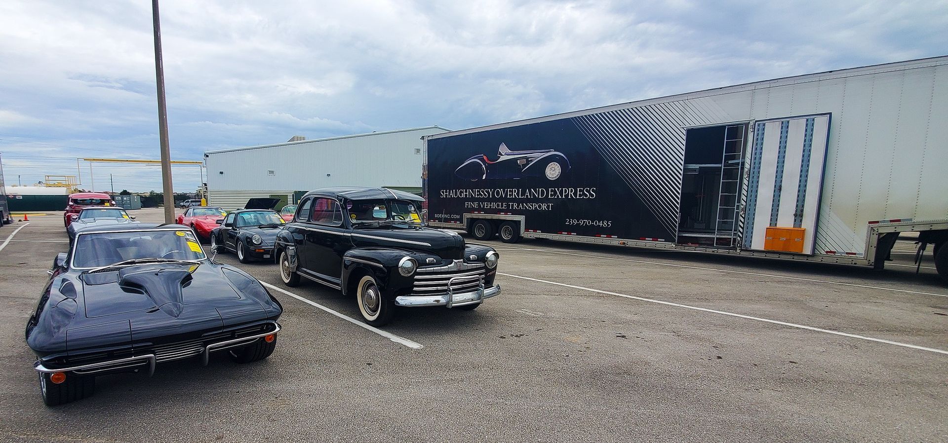 A row of cars are parked in a parking lot next to a train car.