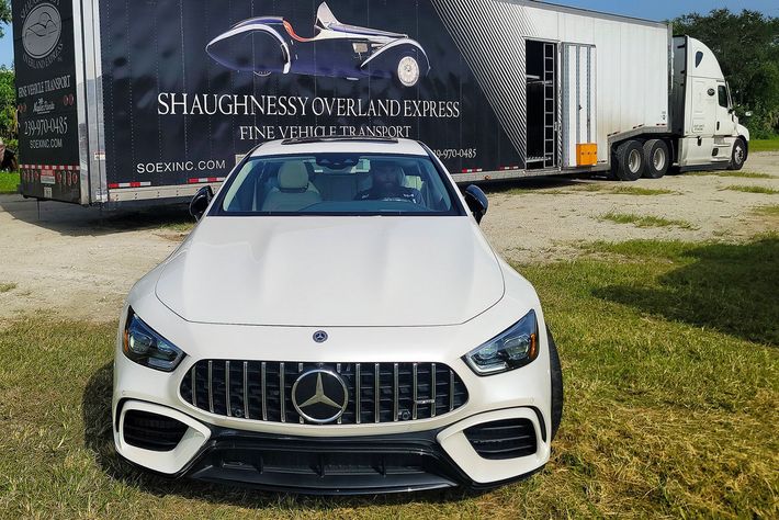 A white mercedes benz is parked in front of a trailer.