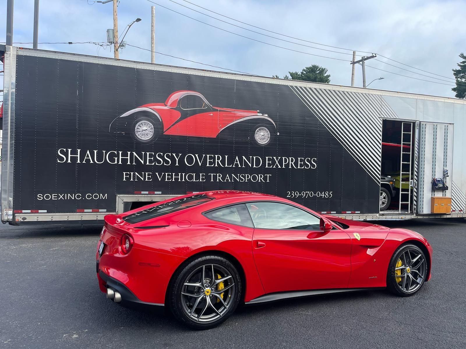 A red sports car is parked in front of a truck that says slaughnessy overland express