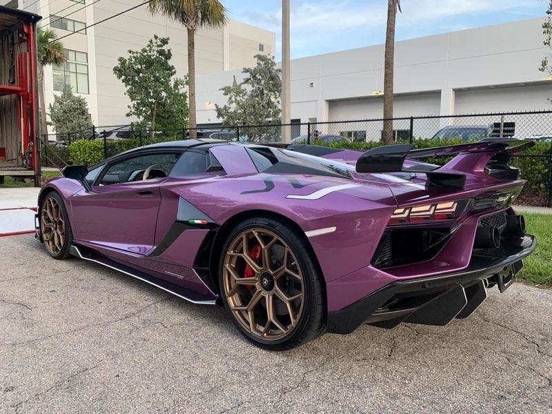 A purple lamborghini aventador is parked in a parking lot.