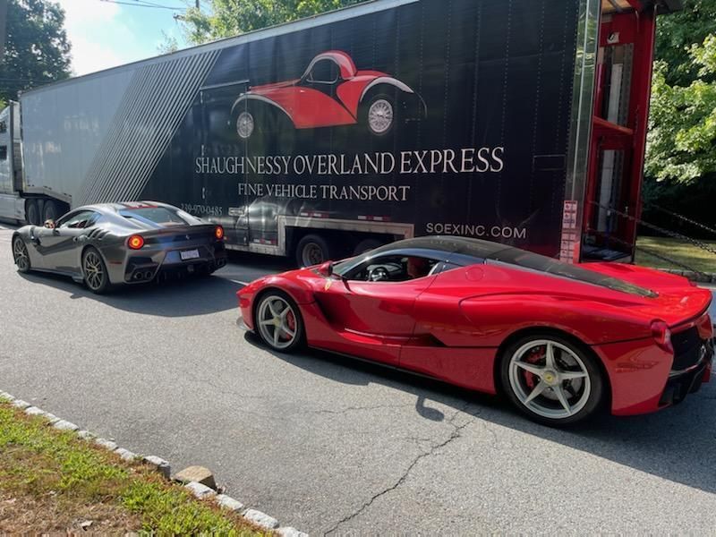 Two sports cars are parked next to a truck that says singleness overland express.