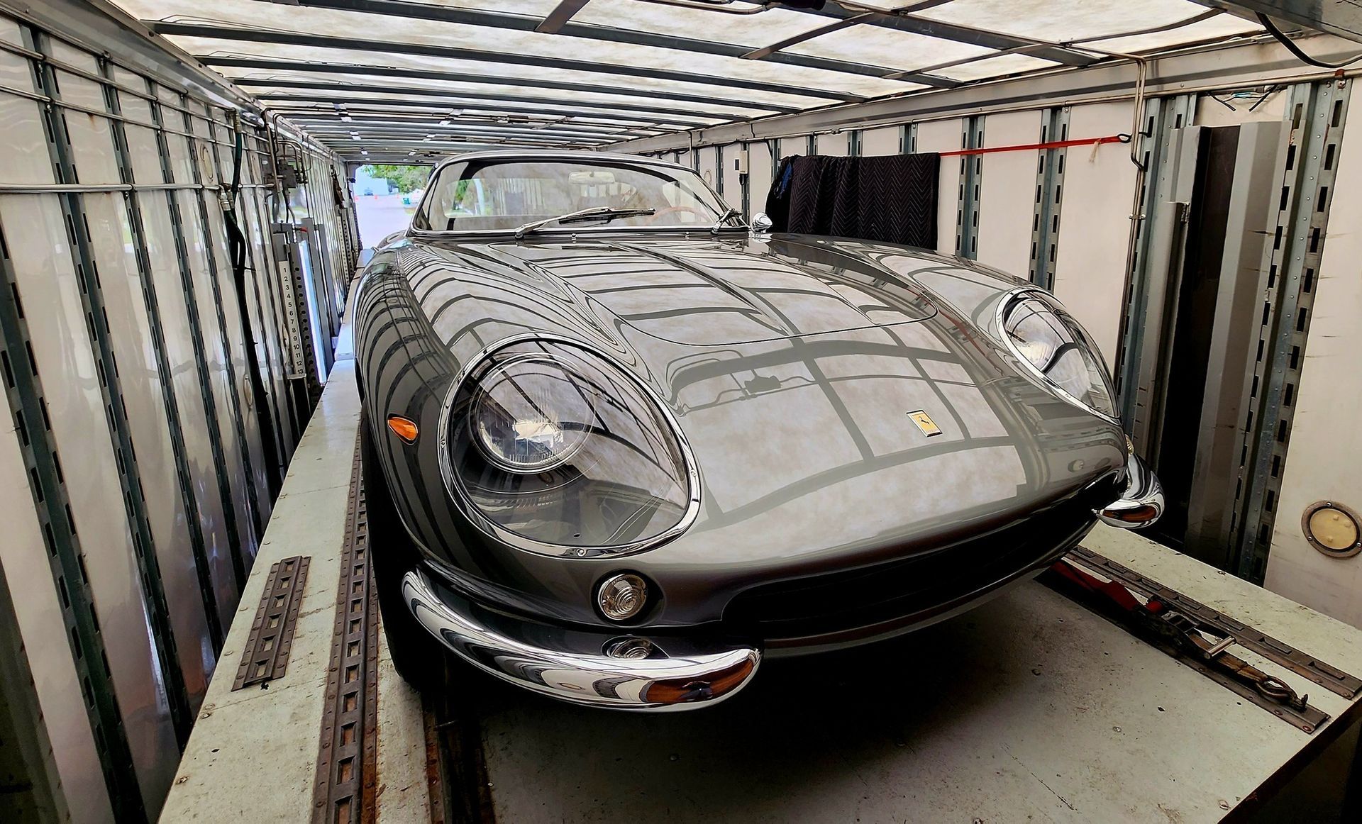 A gray sports car is sitting inside of a shipping container.