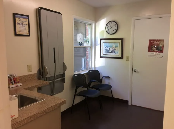 Waiting area with sink, changing station, chairs, clock, art, and door.