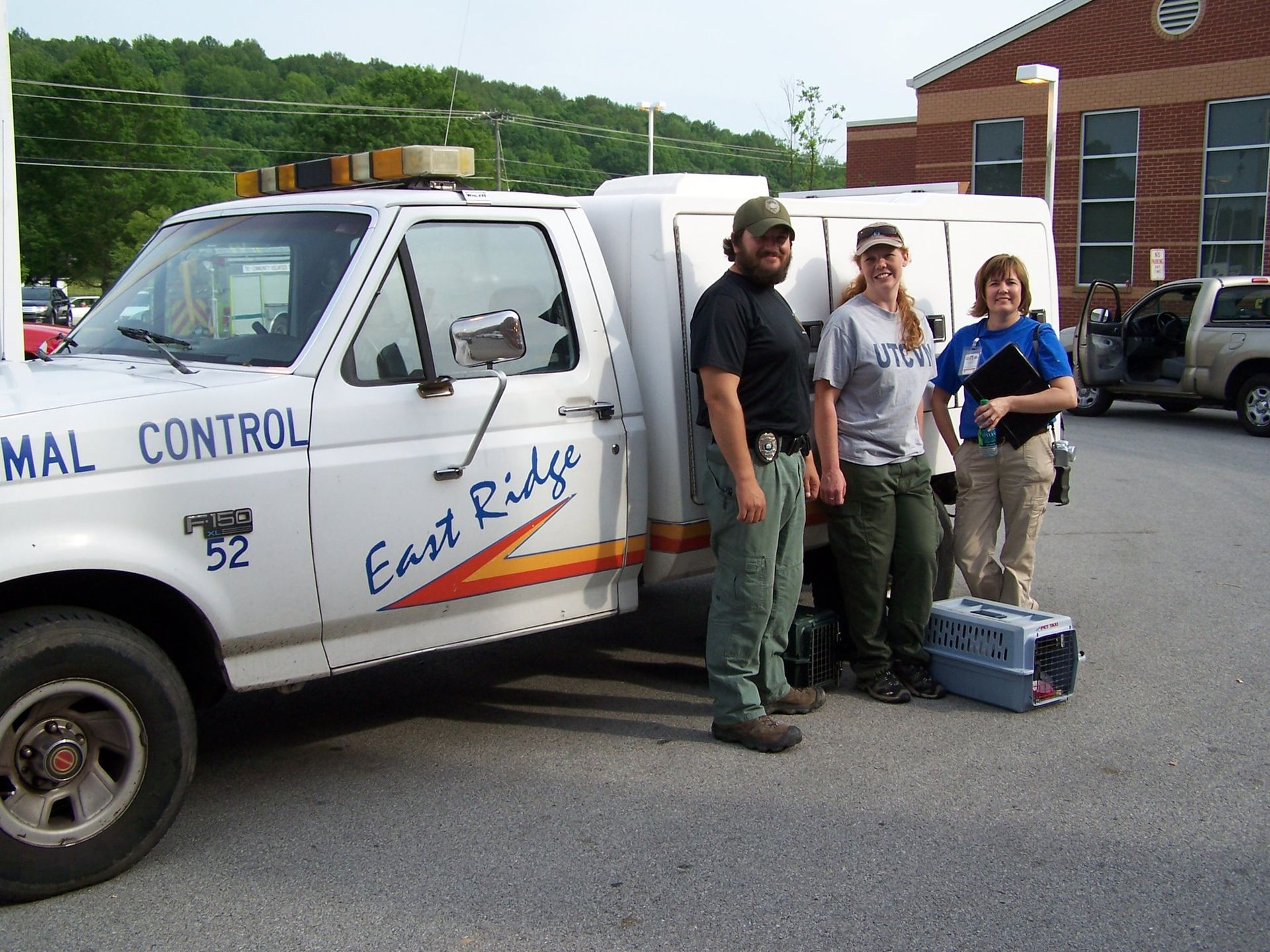 Three animal control officers beside a white truck; East Ridge logo, a building in the background.