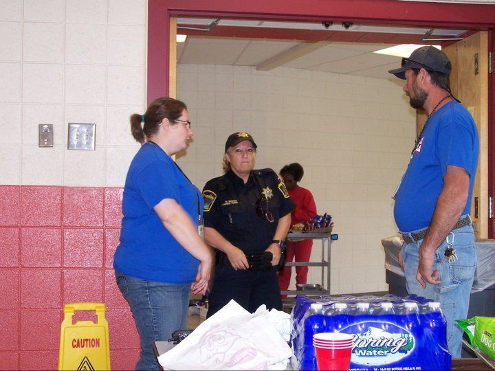 Three people talking: woman in blue, police officer, man in blue, inside a building.