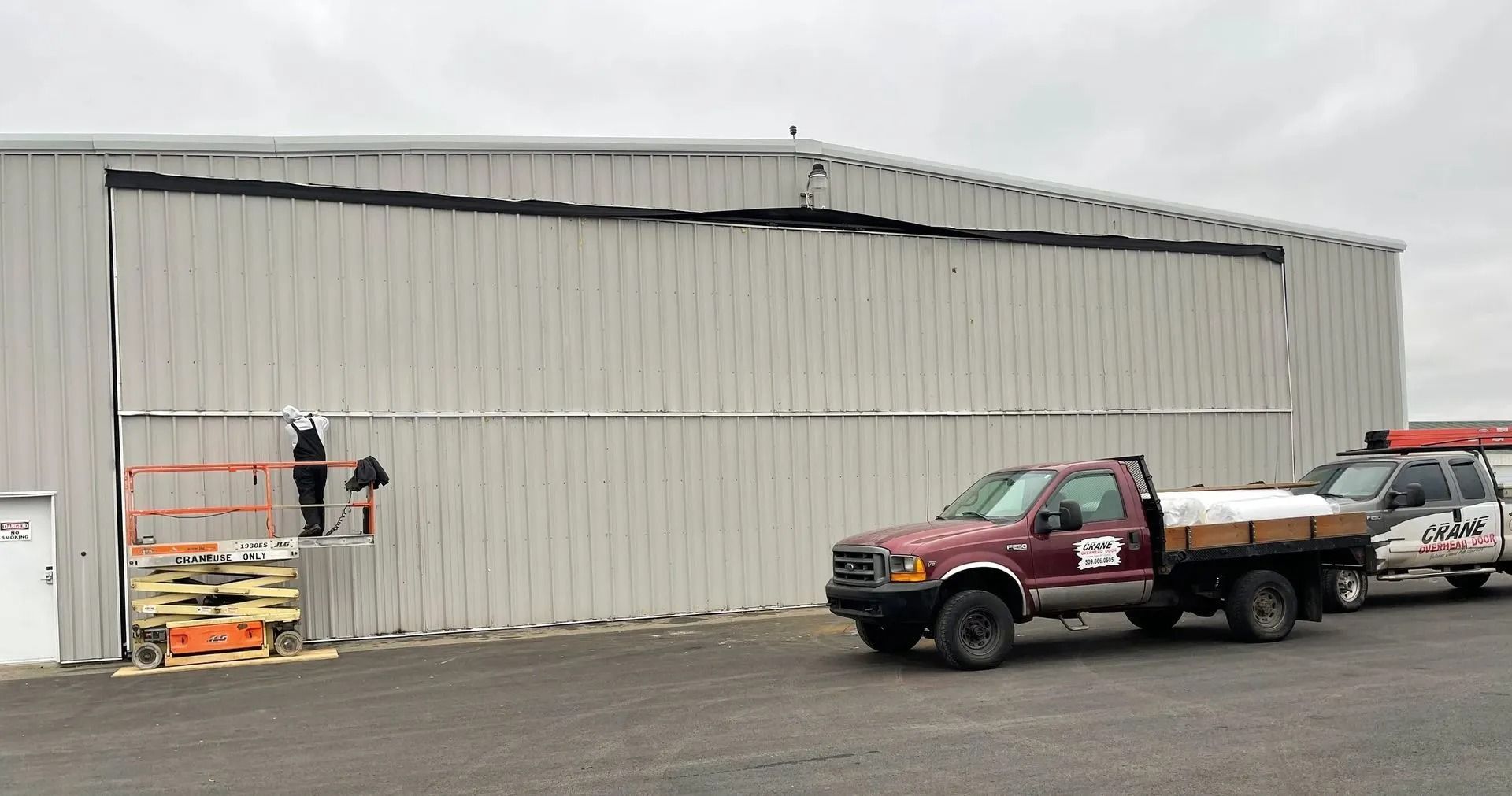 A three-car garage with white paneled doors and window inserts, located beside a house with gray and wood-shingled siding.