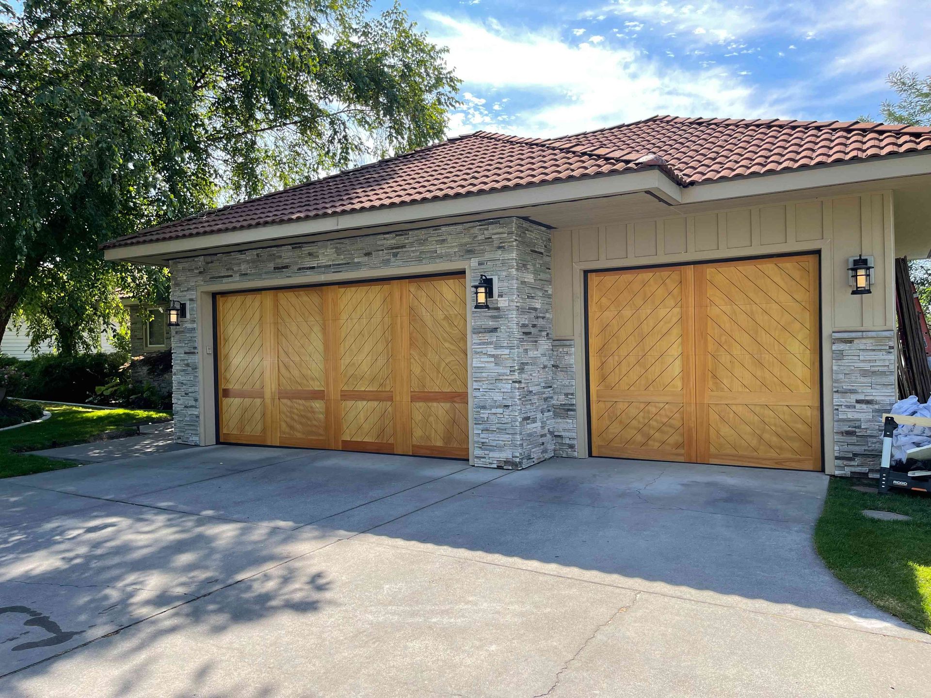 A three-car garage with light wood doors, decorative lattice panels, and stone siding under a dark tile roof.
