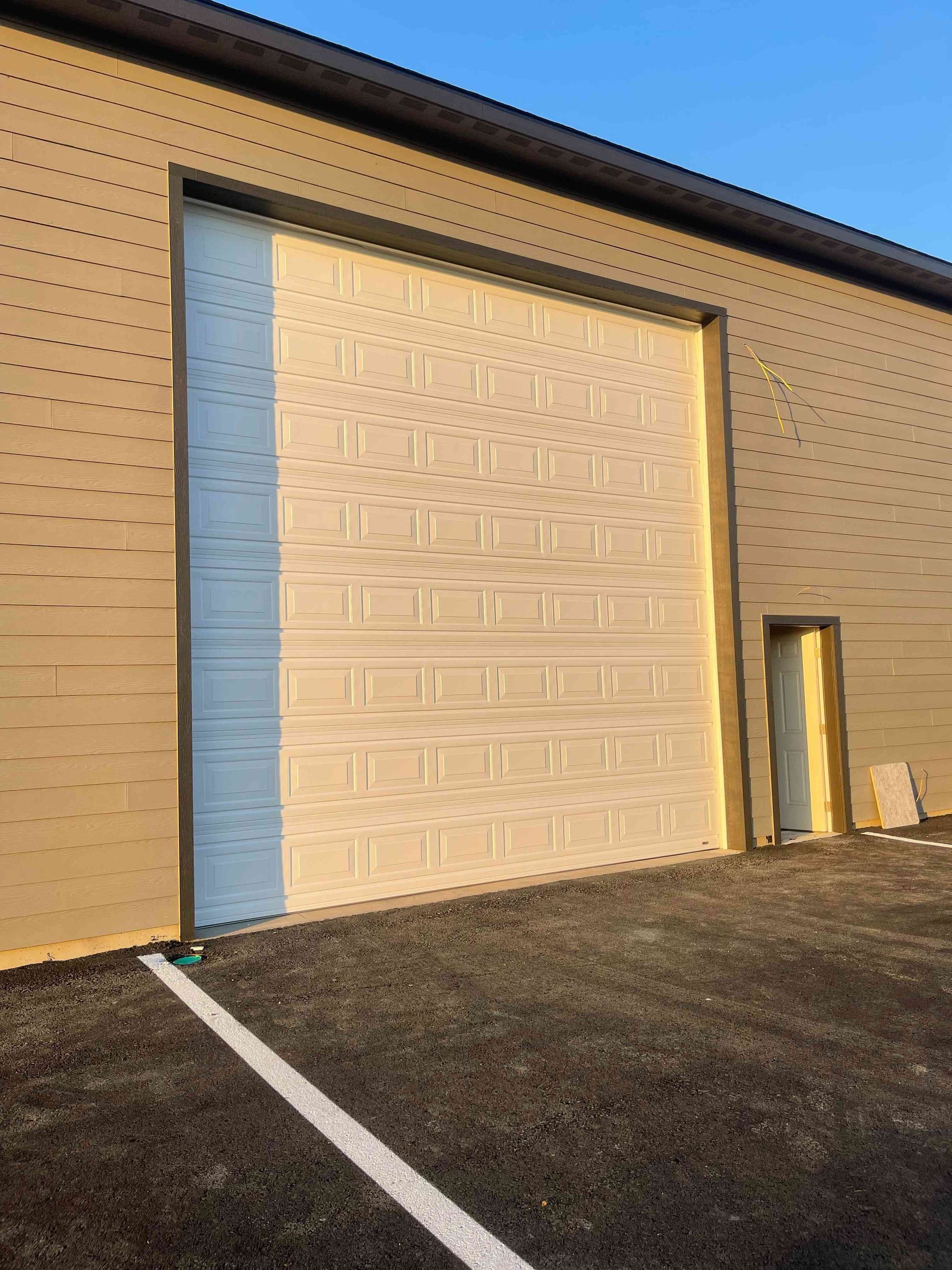 A white sectional garage door set into the tan-sided wall of a commercial building, next to a standard entry door.