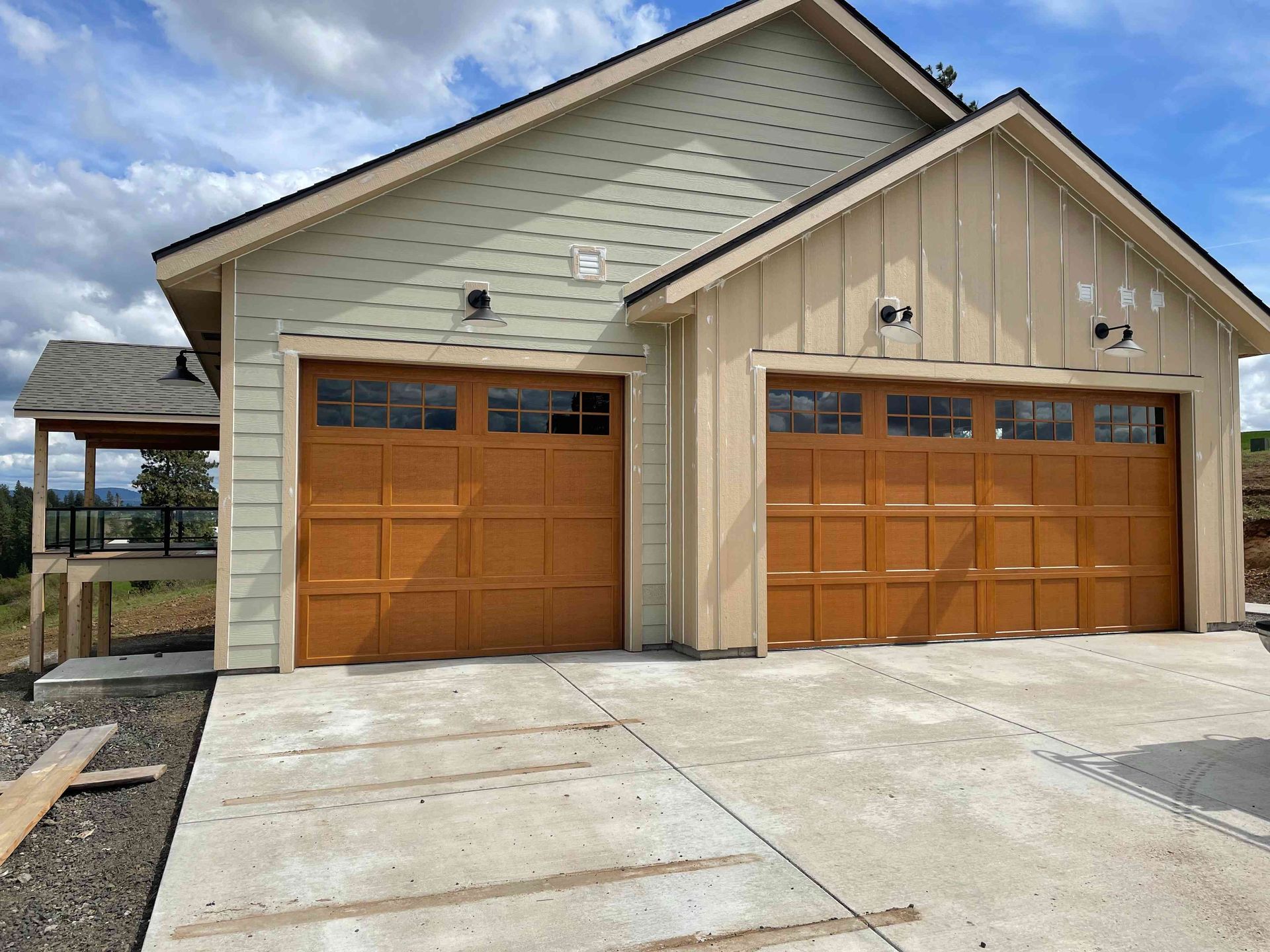 A detached garage with two wooden doors, light green and tan siding, and an attached side porch under a cloudy sky.