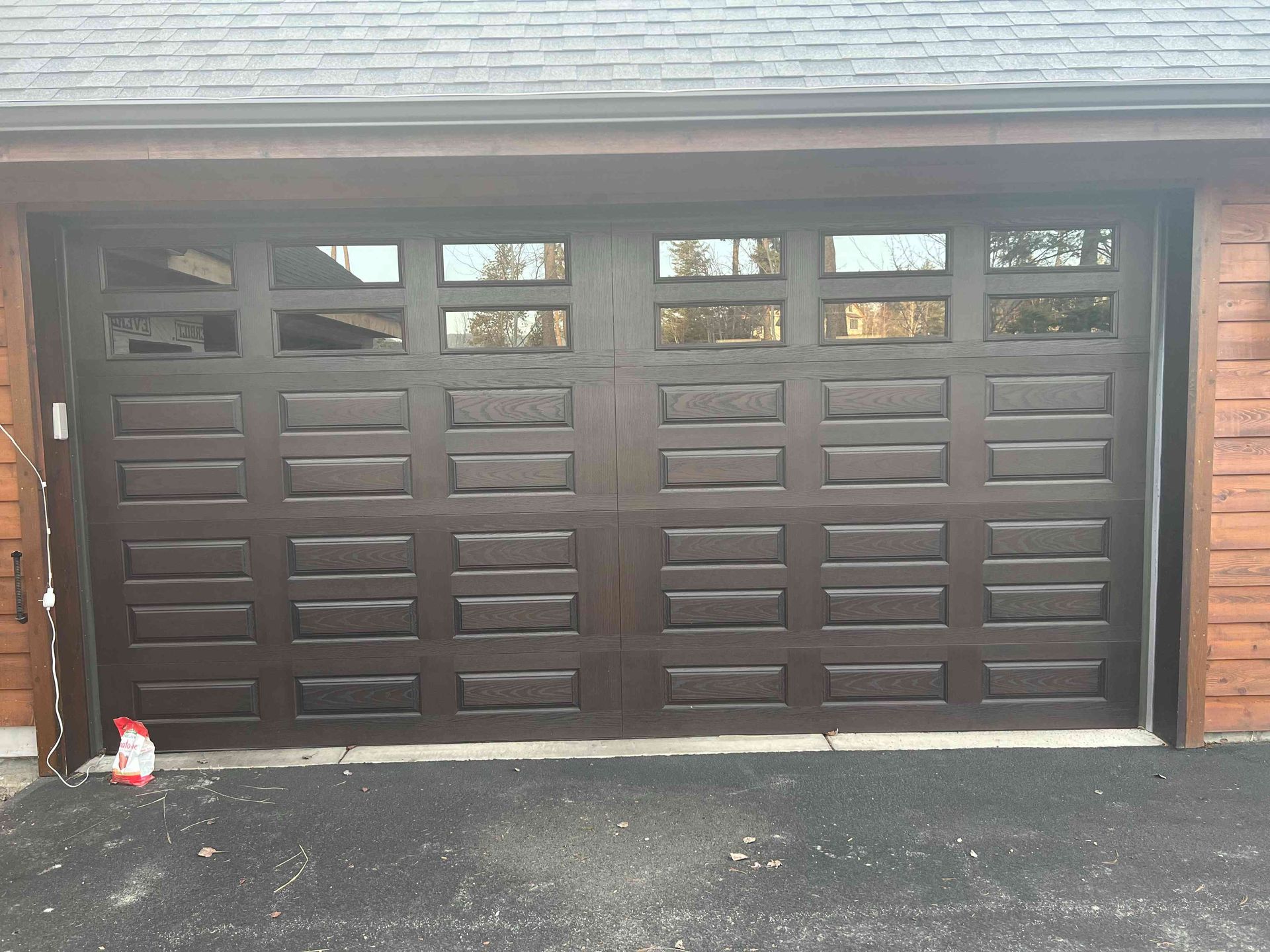 A dark brown, multi-panel residential garage door with a row of rectangular windows along the top.