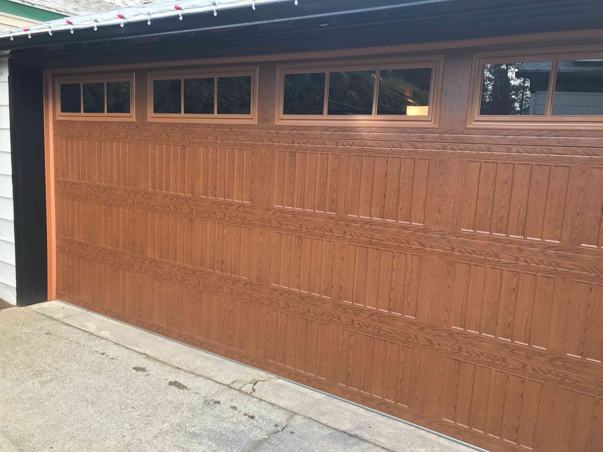 A brown garage door with a wood grain finish, featuring a row of four rectangular windows at the top.