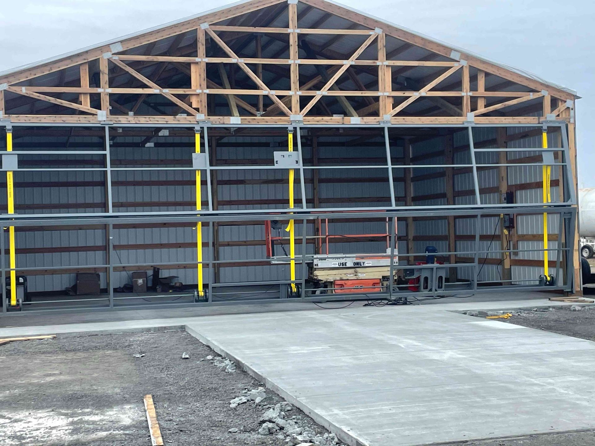 A large, metal-framed pole barn under construction with a yellow hydraulic door lift system installed in the opening.