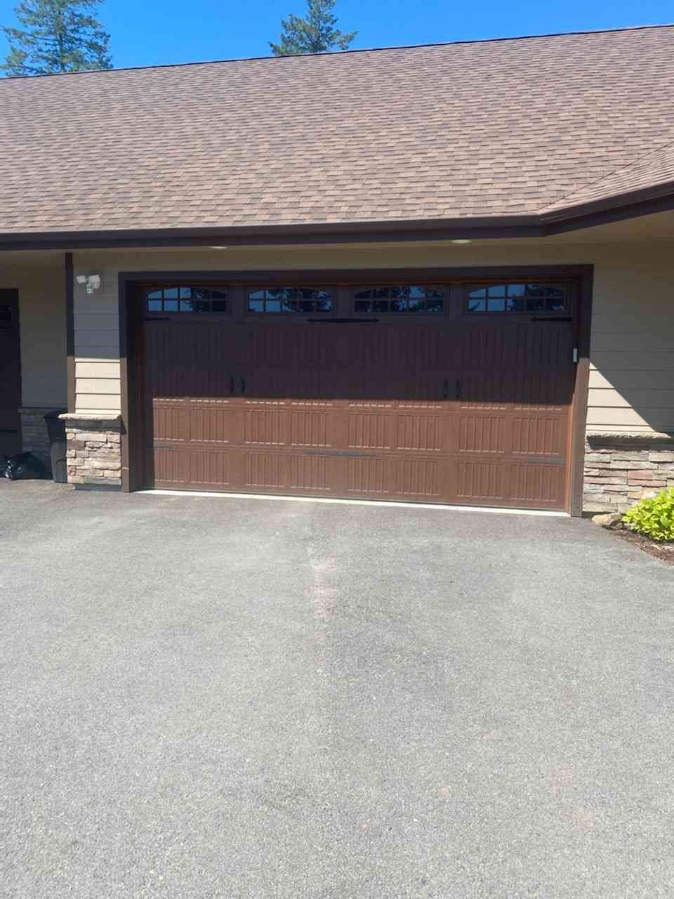 A brown garage door with rectangular window panels on a residential building with a paved driveway.