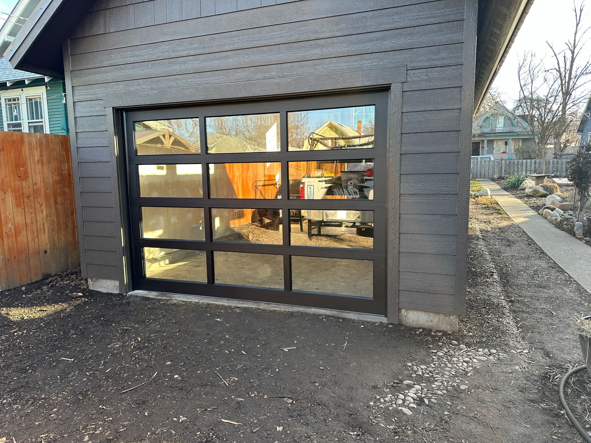 A modern dark-framed glass garage door installed on a garage with brown wood siding.