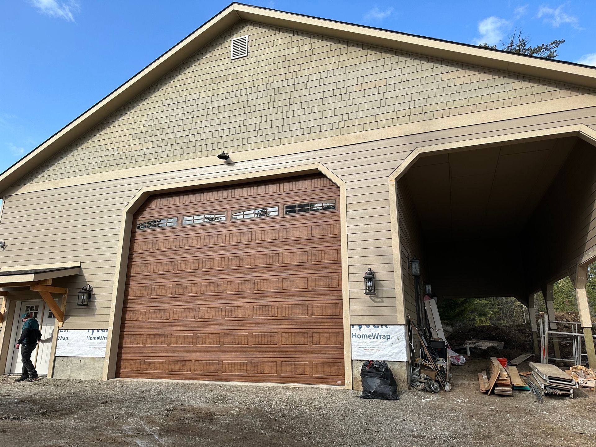 A garage with tan siding and a brown wooden garage door, with an open side bay and a person standing near a side door.
