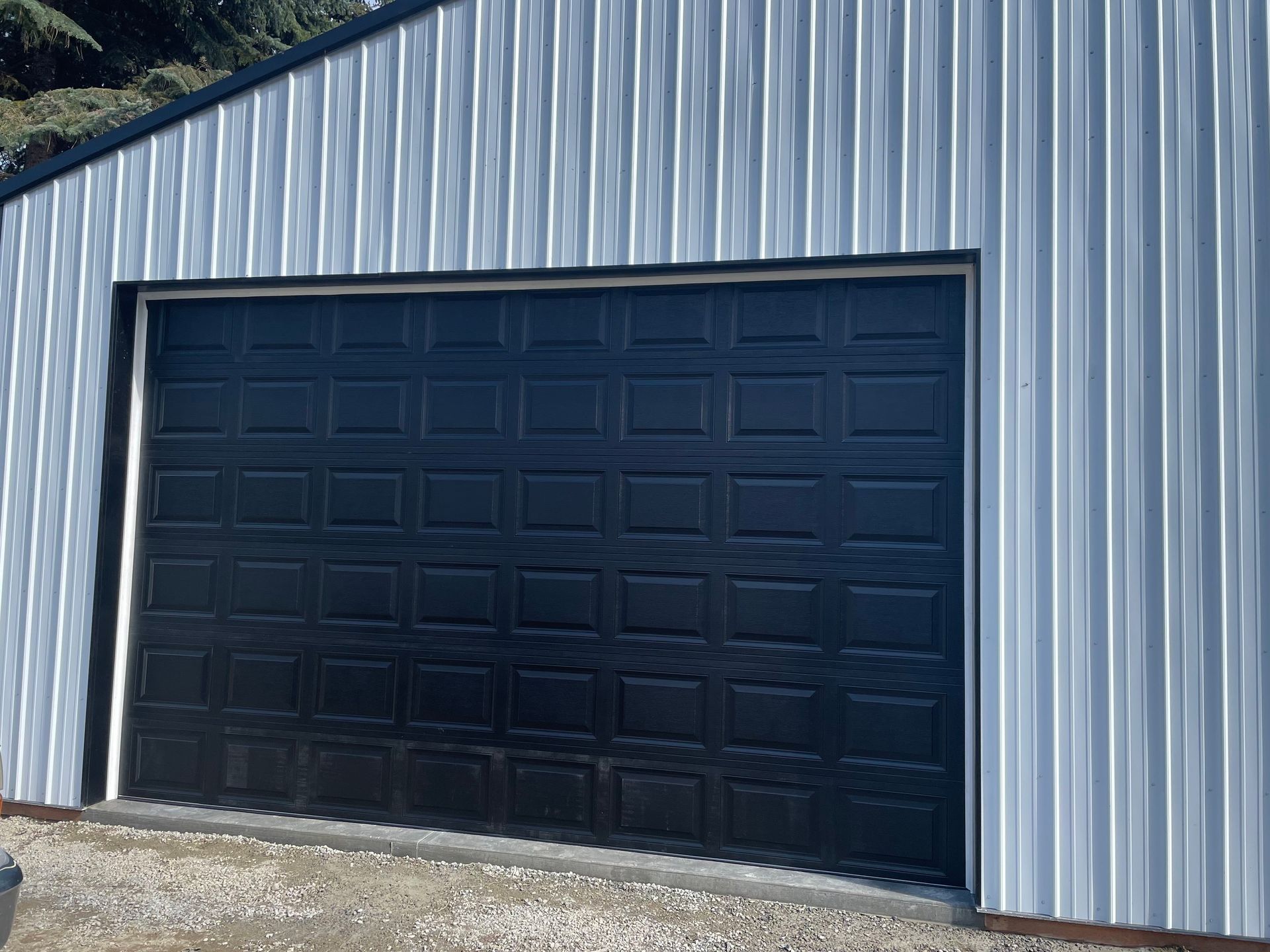 A black rectangular garage door centered on the wall of a building with light gray vertical metal siding.
