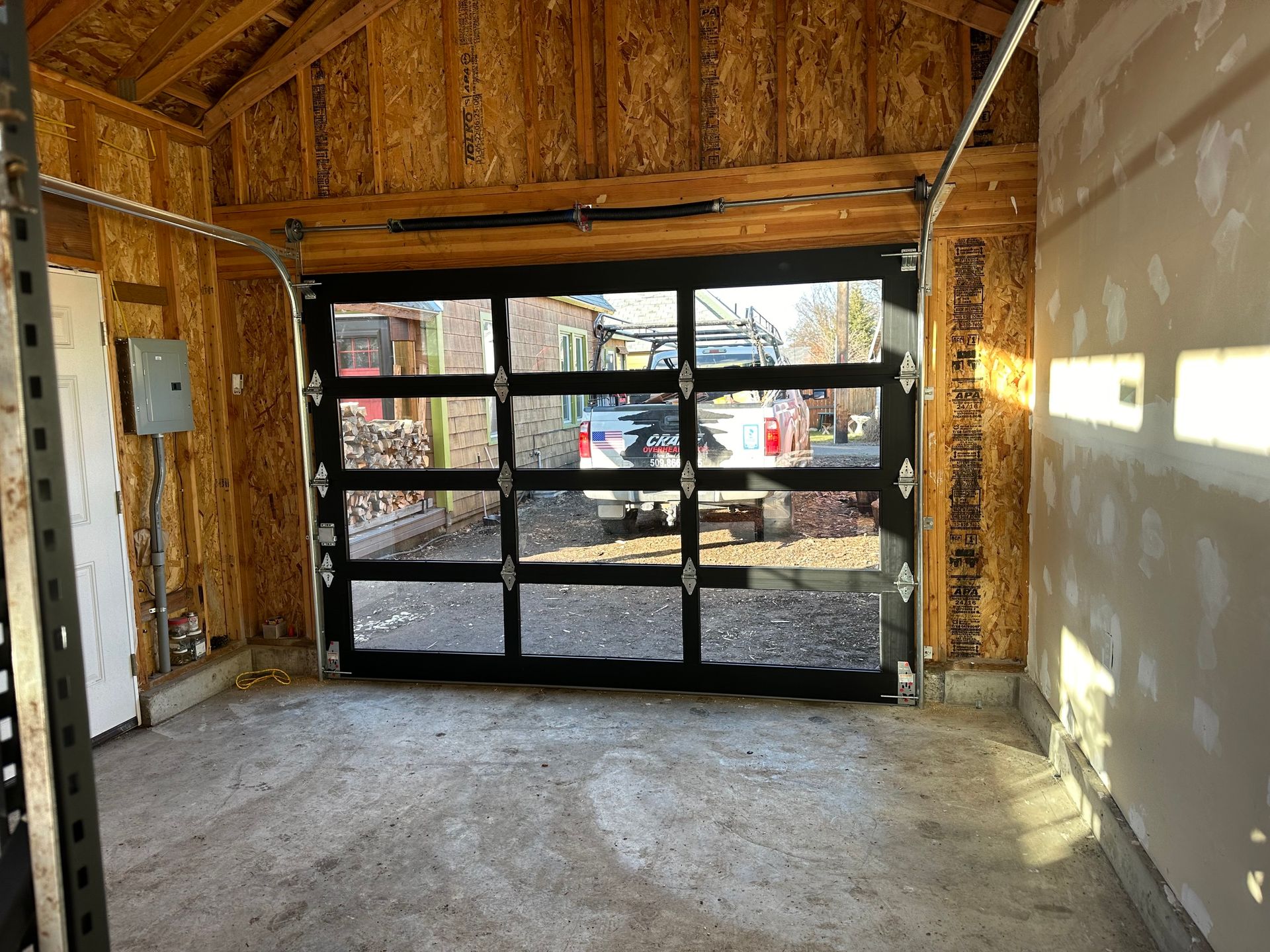 Interior view of a garage featuring a modern, black-framed glass sectional garage door looking out onto a driveway.