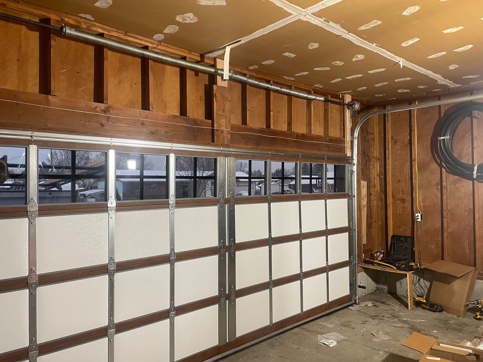 An interior view of a garage door with windows, showing its white panels, metal frame, and surrounding wooden wall studs.