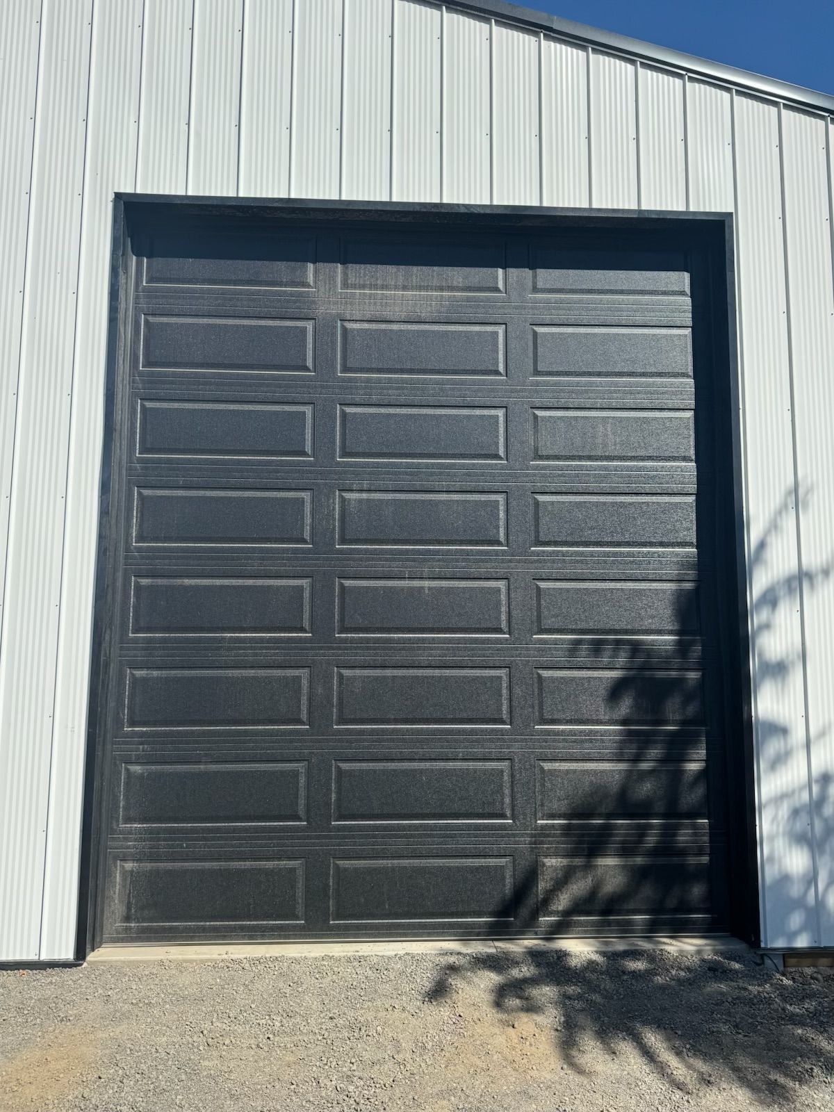 A black, multi-panel garage door installed on a building with white, vertical metal siding.