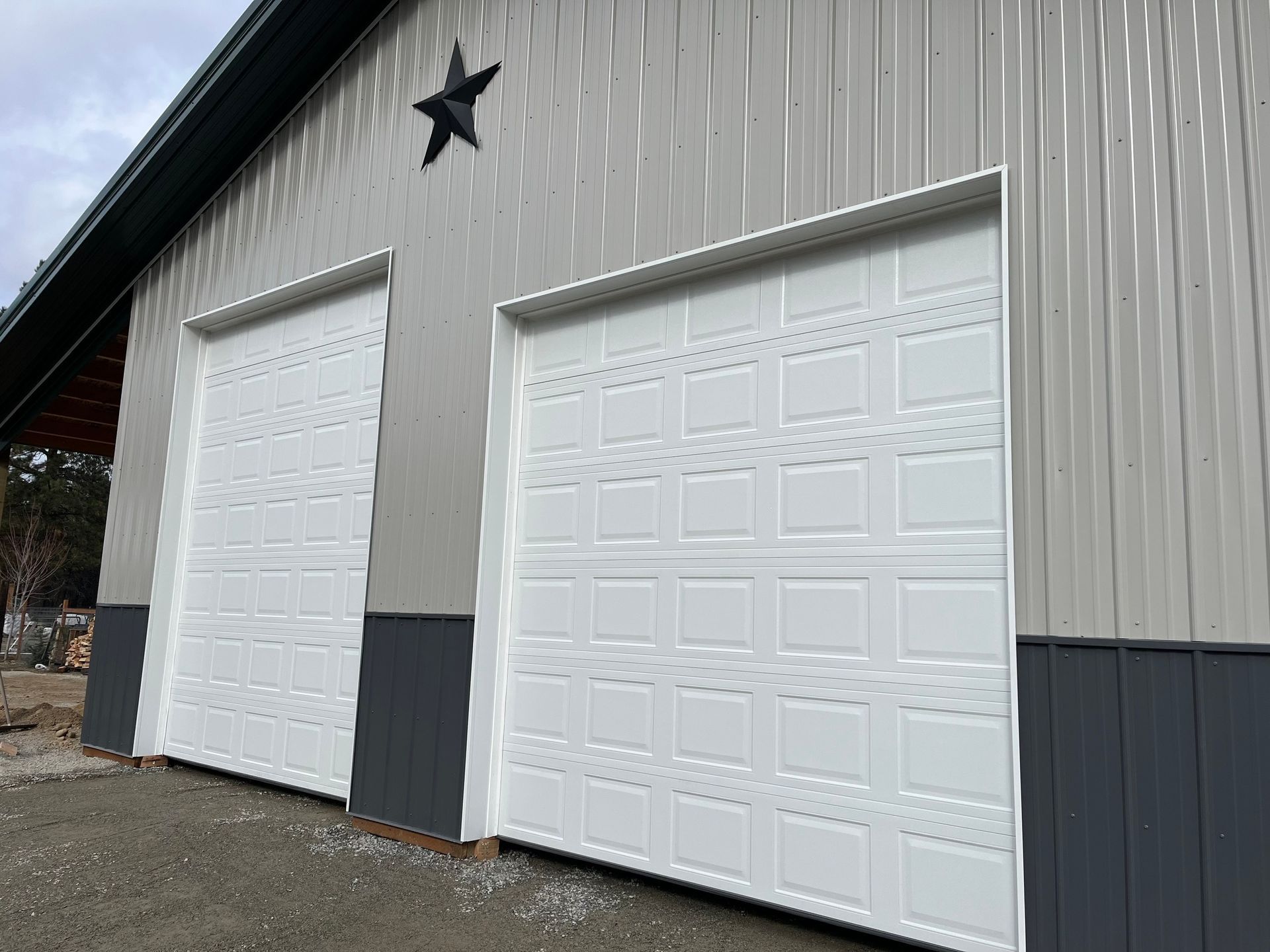 A metal barn exterior with two white sectional garage doors and a decorative black star mounted on the gray siding.