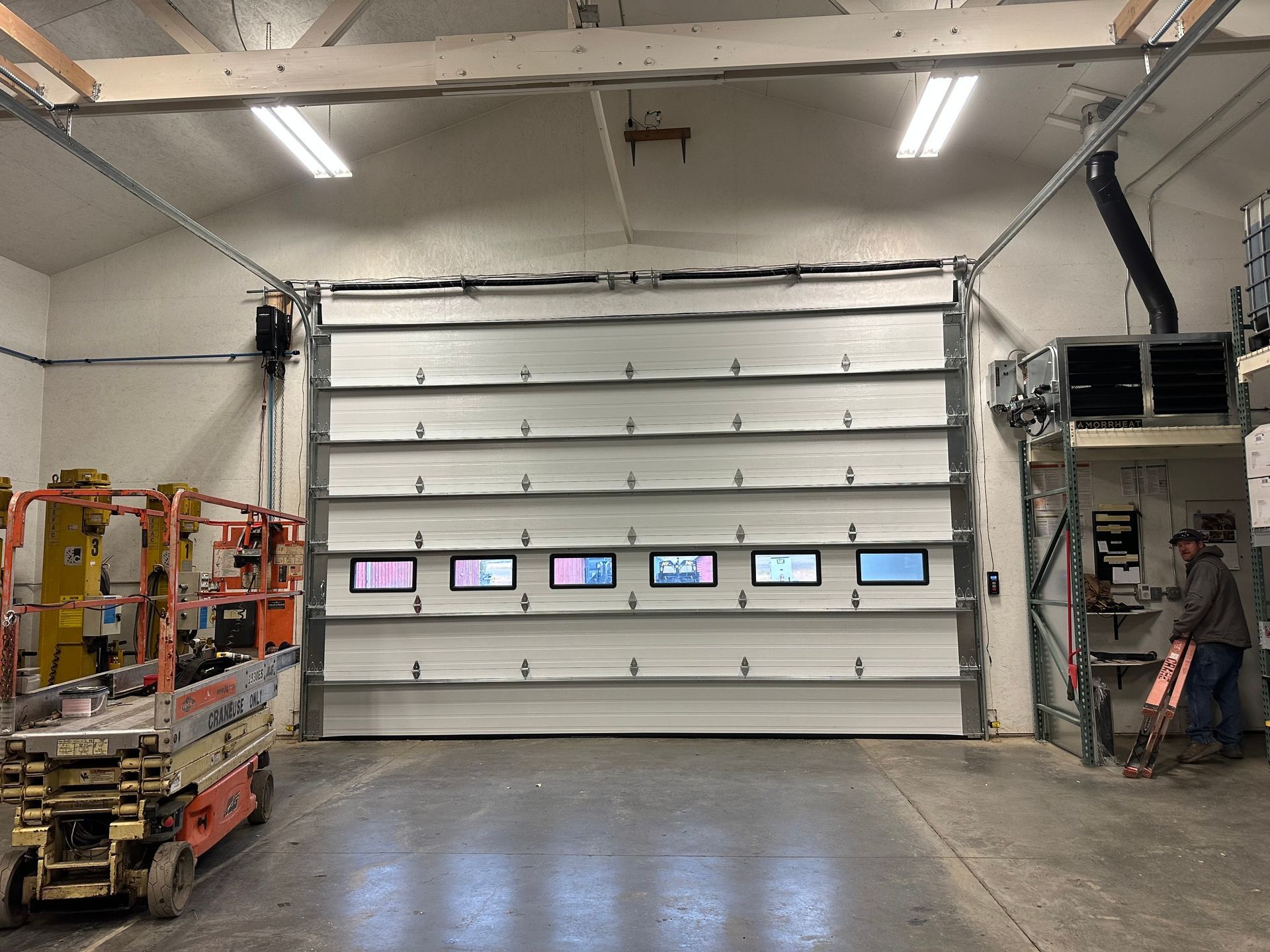 A large, white sectional garage door with a row of six windows in an industrial workshop space.