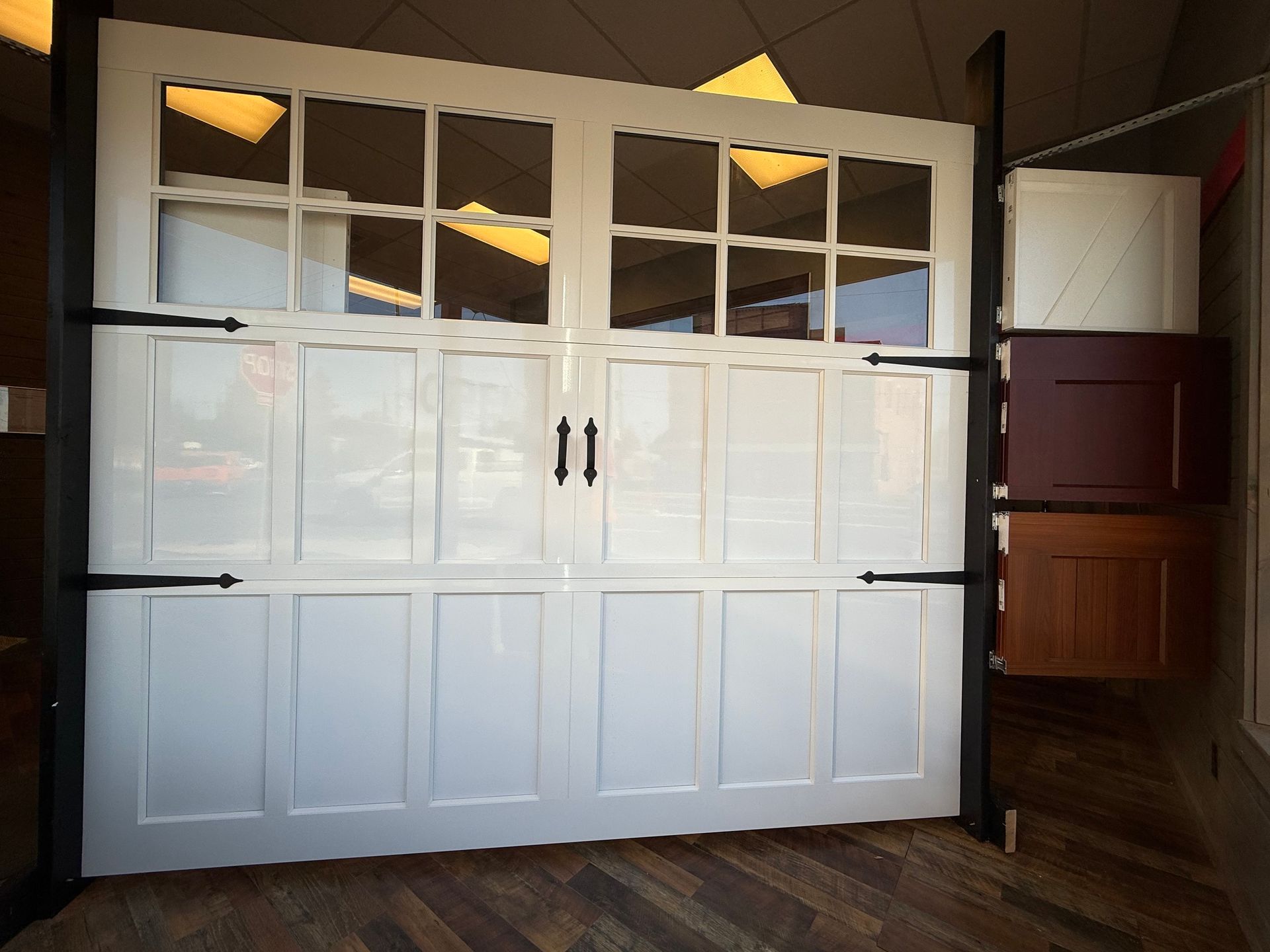 A white, multi-paneled garage door display with windows and black hardware inside a showroom.