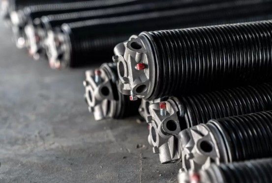 A row of black metal garage door torsion springs resting on a concrete floor.