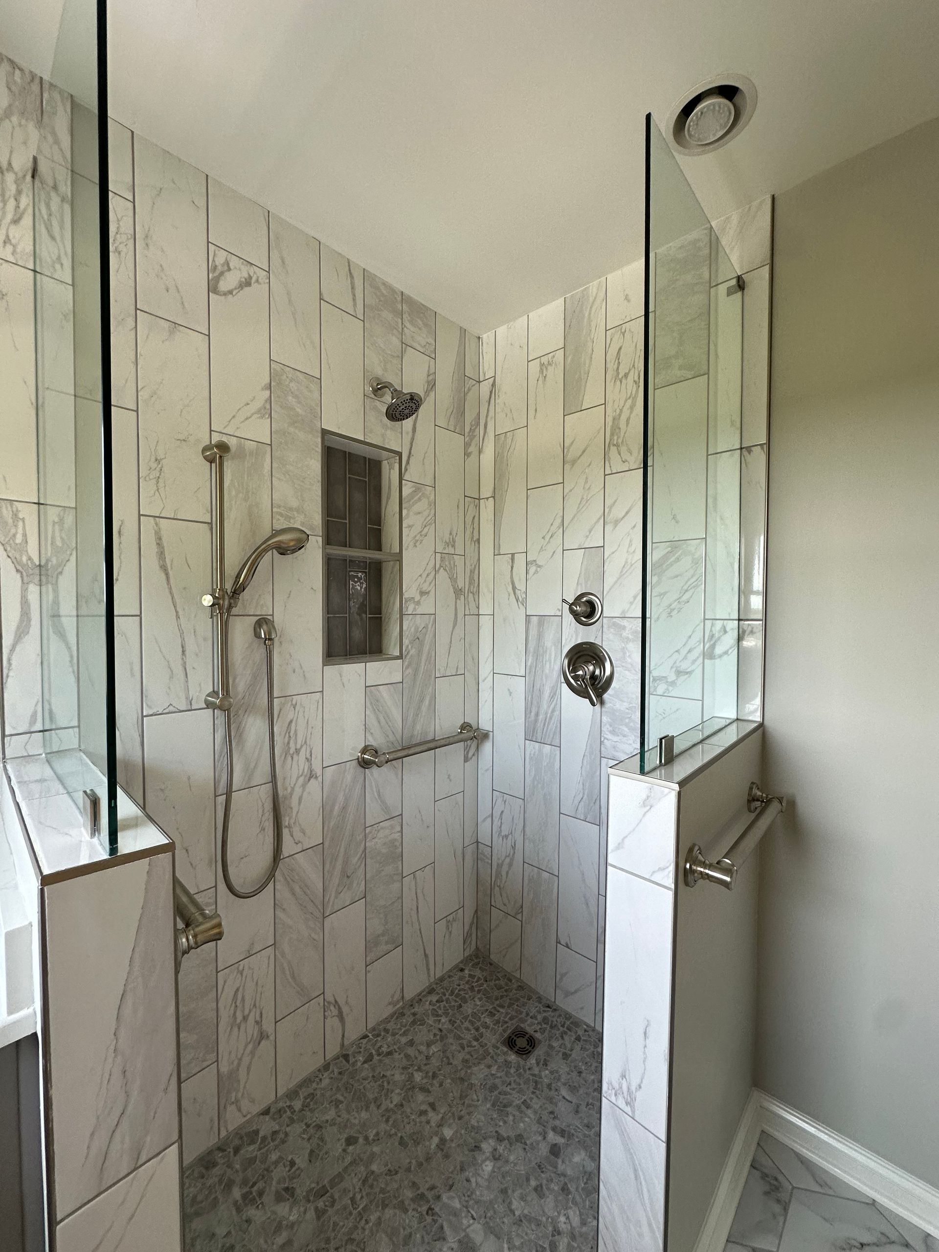 A bathroom with marble tiles and a walk in shower with a glass door.