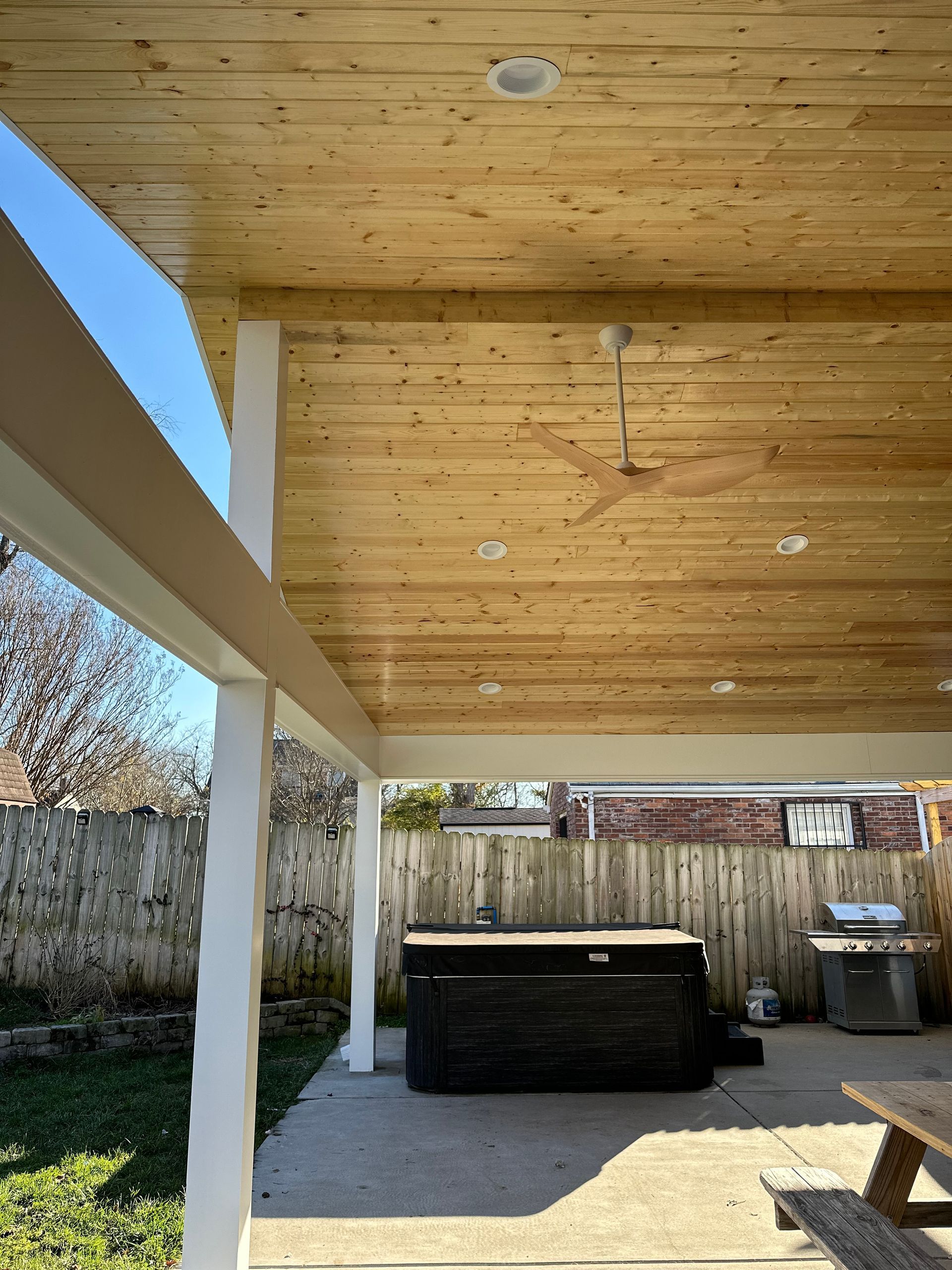 A wooden covered patio with a hot tub and a picnic table.