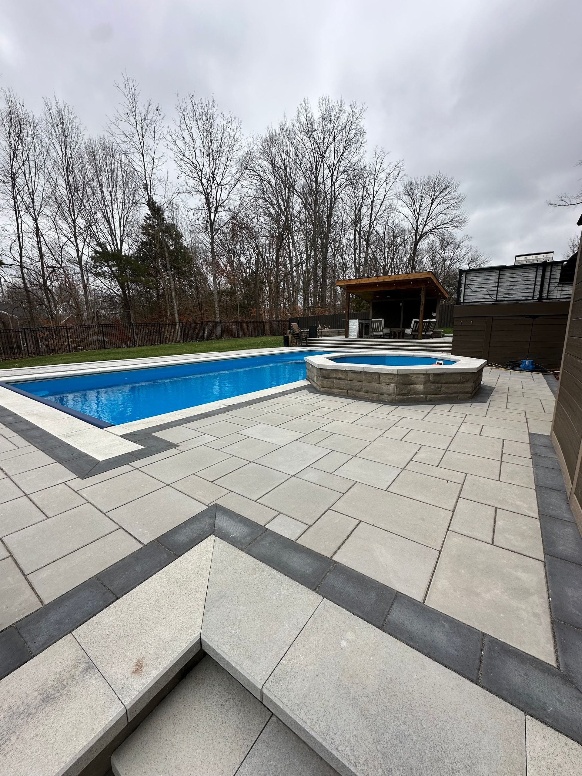 A large swimming pool is surrounded by a patio and trees.