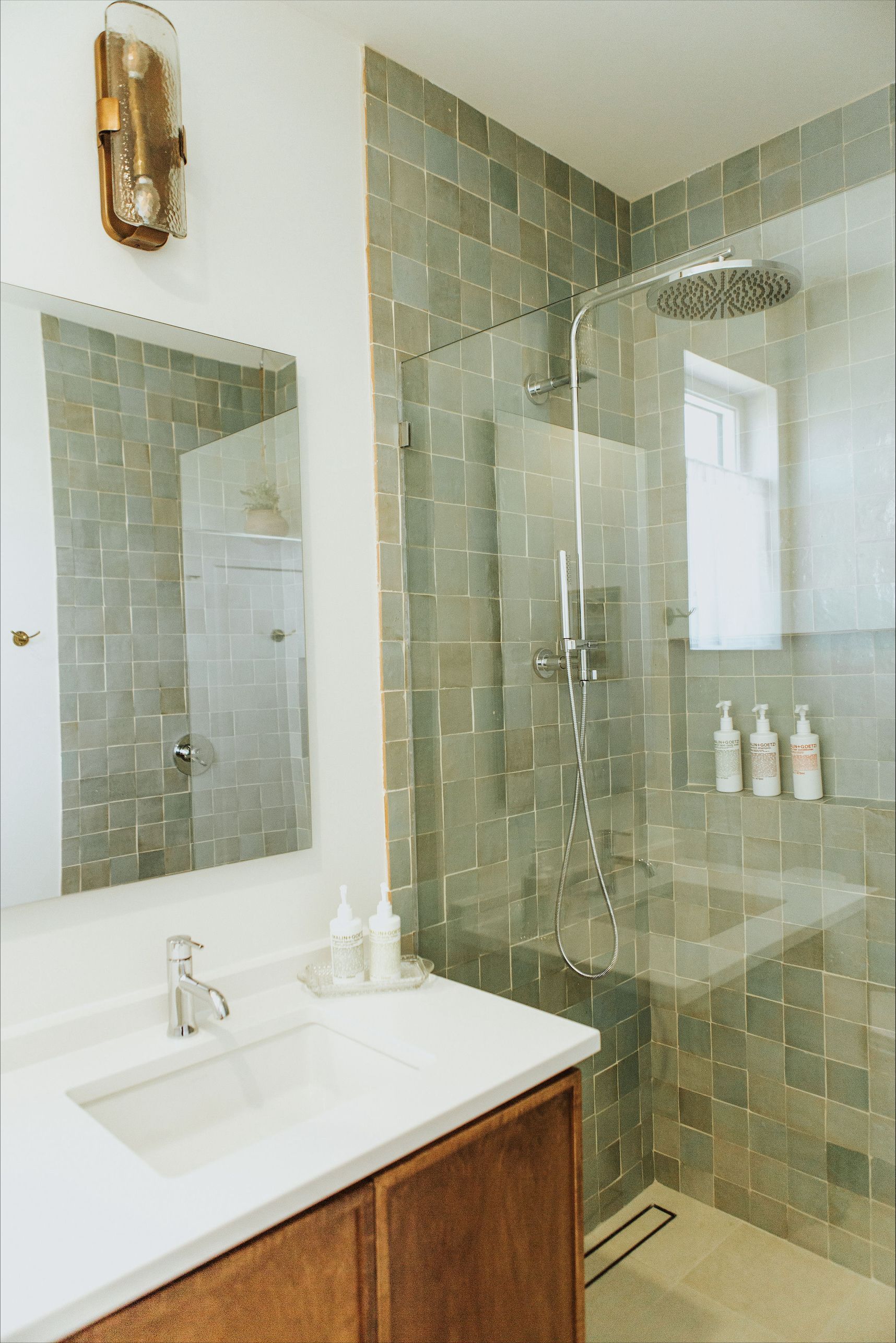 A bathroom with a sink , mirror and walk in shower.