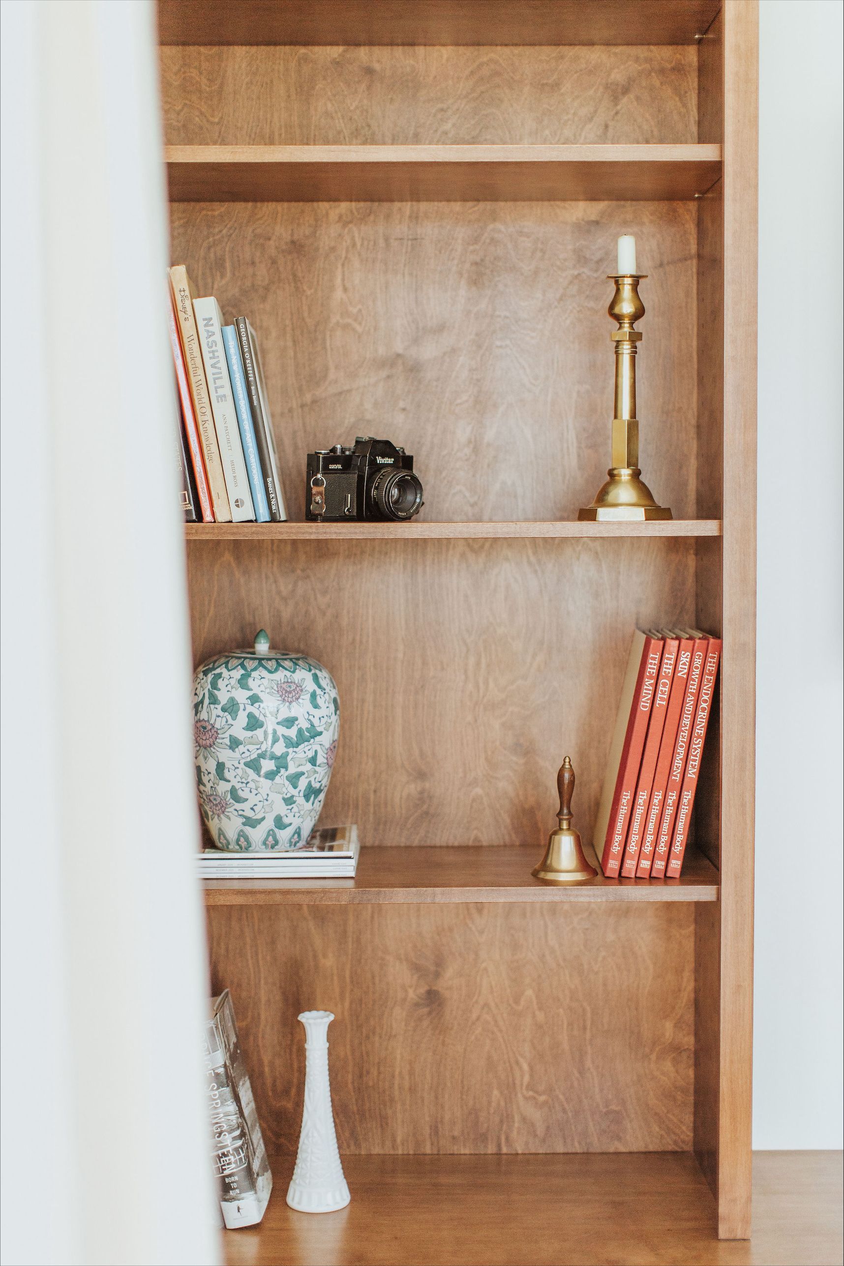 A wooden bookshelf with books , vases , and a candle on it.